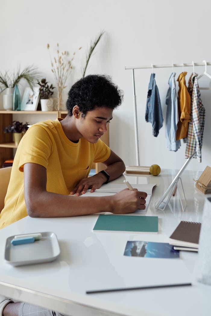 Home Focused African American teen studying indoors with a tablet and notebook at home.