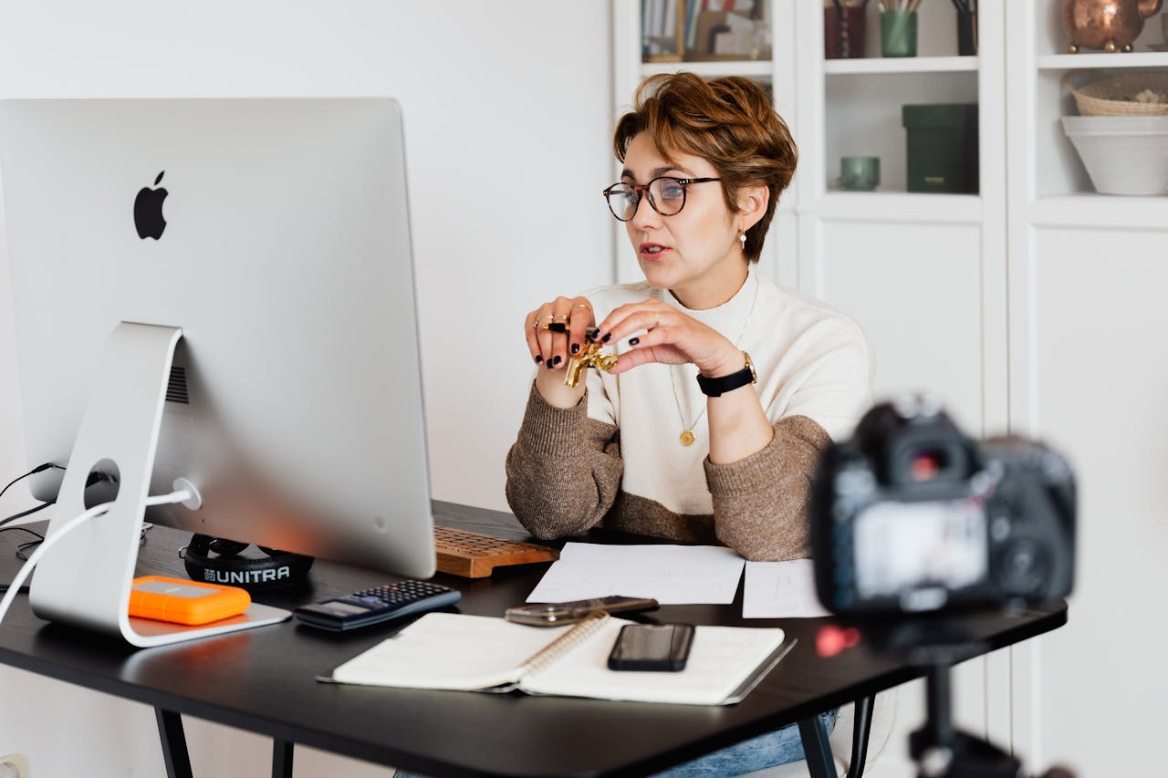 Home A professional woman engaged in a virtual meeting setup at her home desk, using a computer and camera.