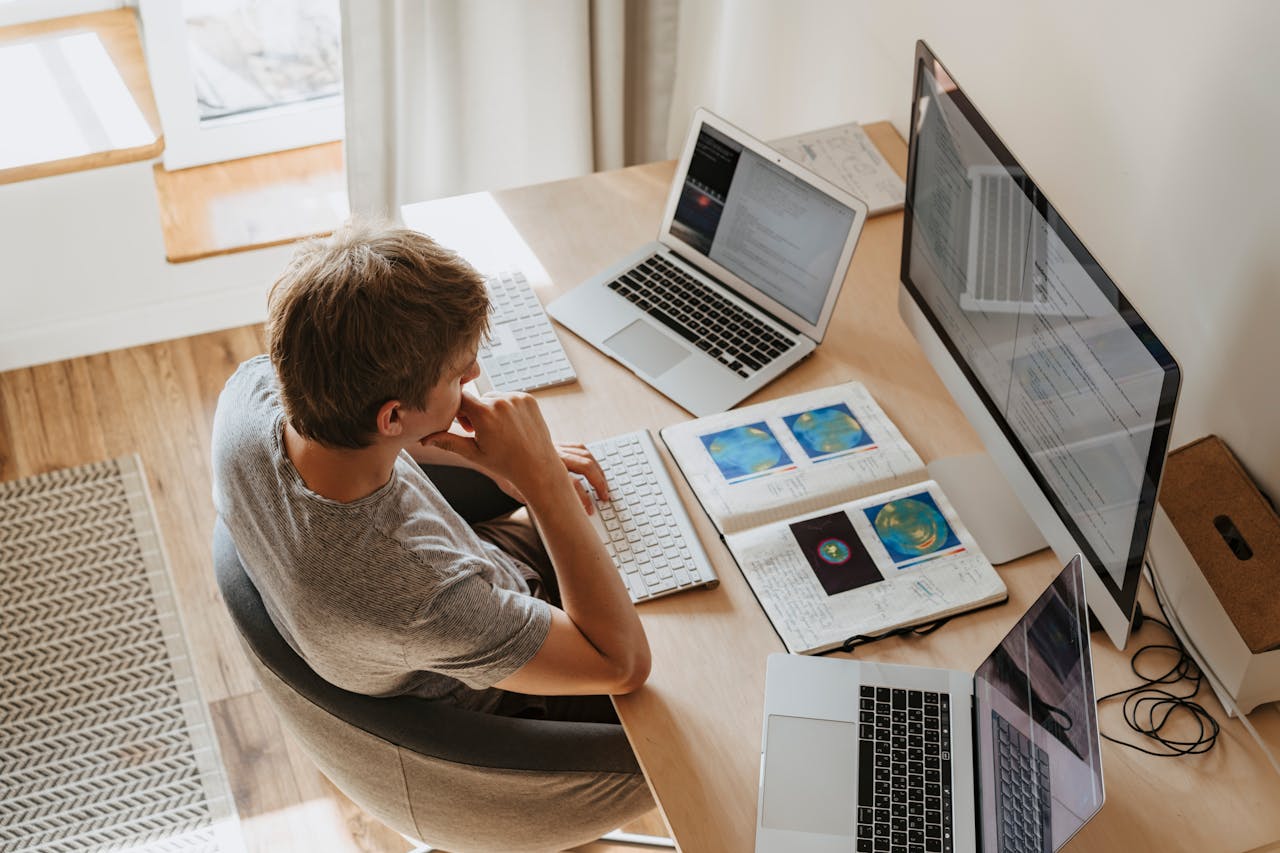 Home Top view of young programmer working on multiple laptops in a modern office setting.
