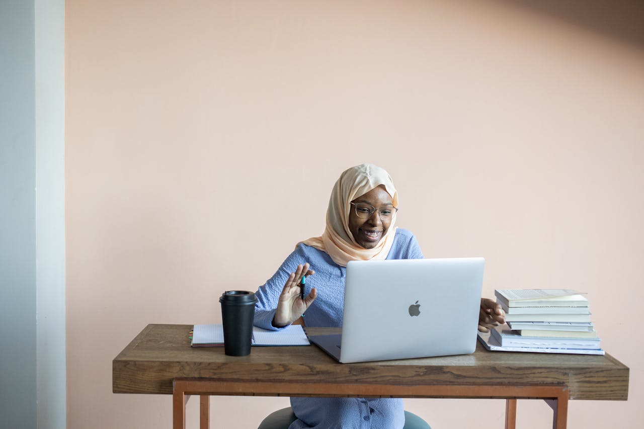 Home Smiling Muslim woman in hijab waving during an online video call.
